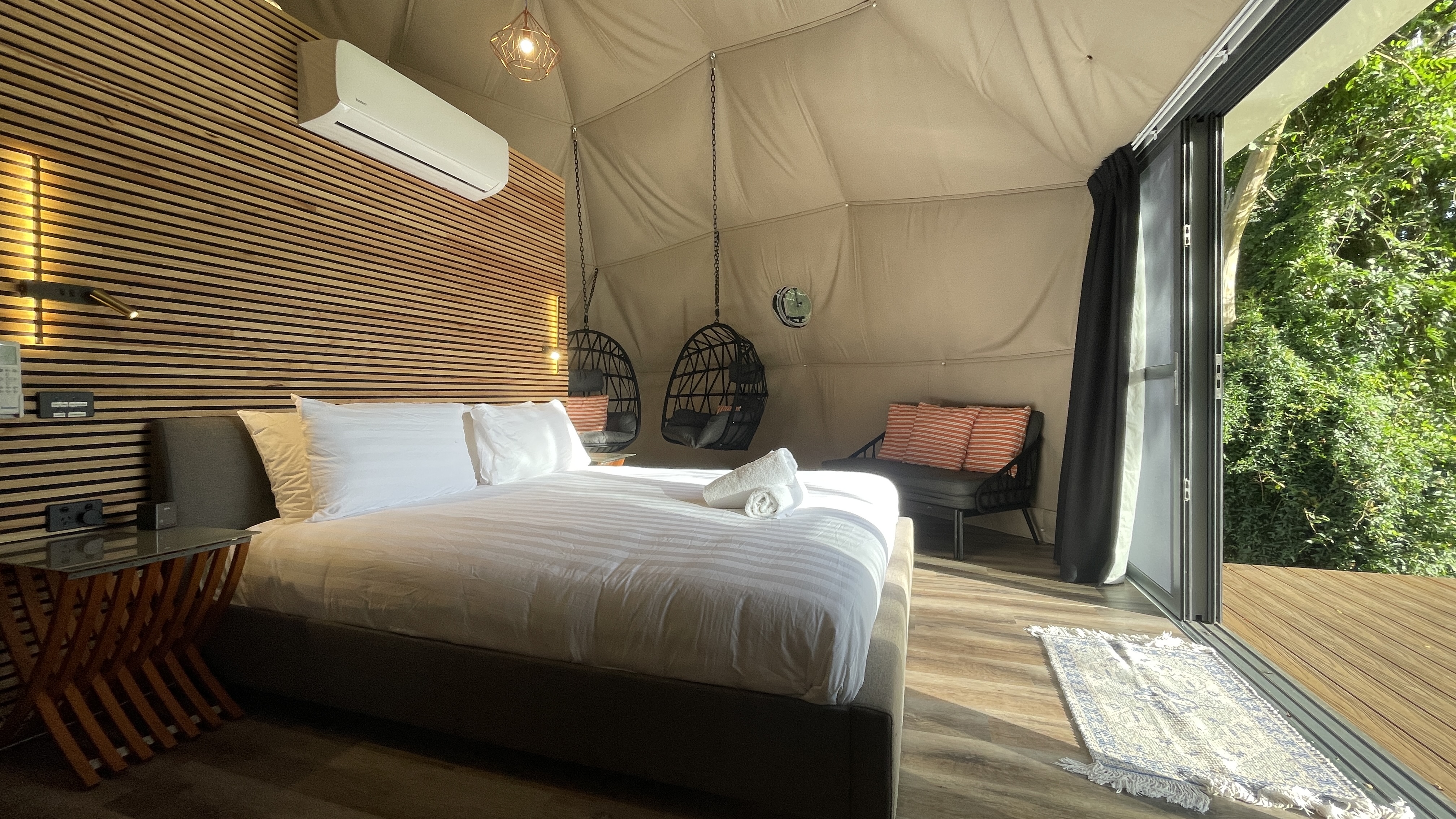 Inside The Nest Glamping Dome: king bed, hanging egg chairs and floor-to-ceiling glass doors
